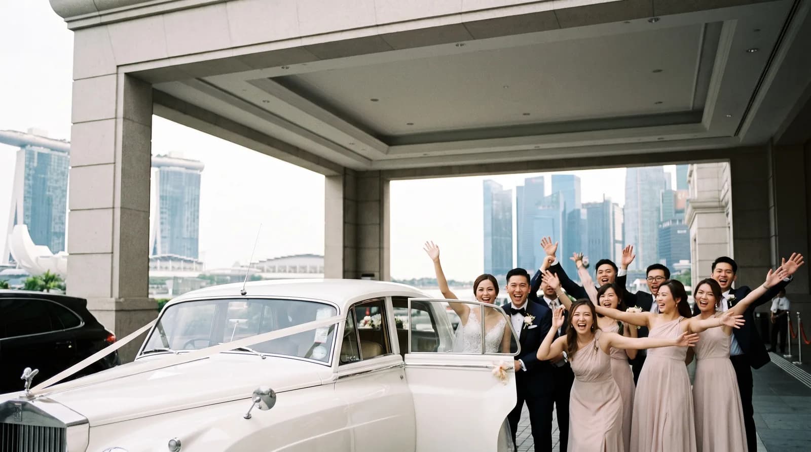 A bridal car arriving at a hotel porte-cochere with the bridal party cheering