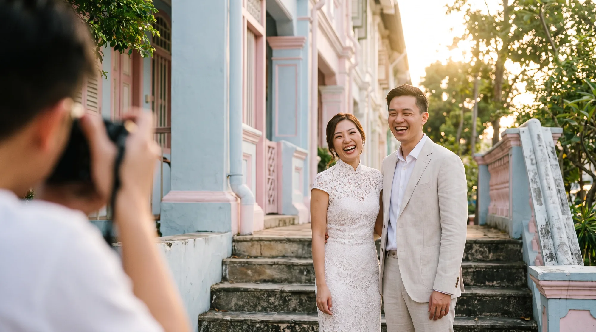 A Singaporean Chinese bride and groom laughing on the steps of a pastel heritage shophouse in Joo Chiat at golden hour